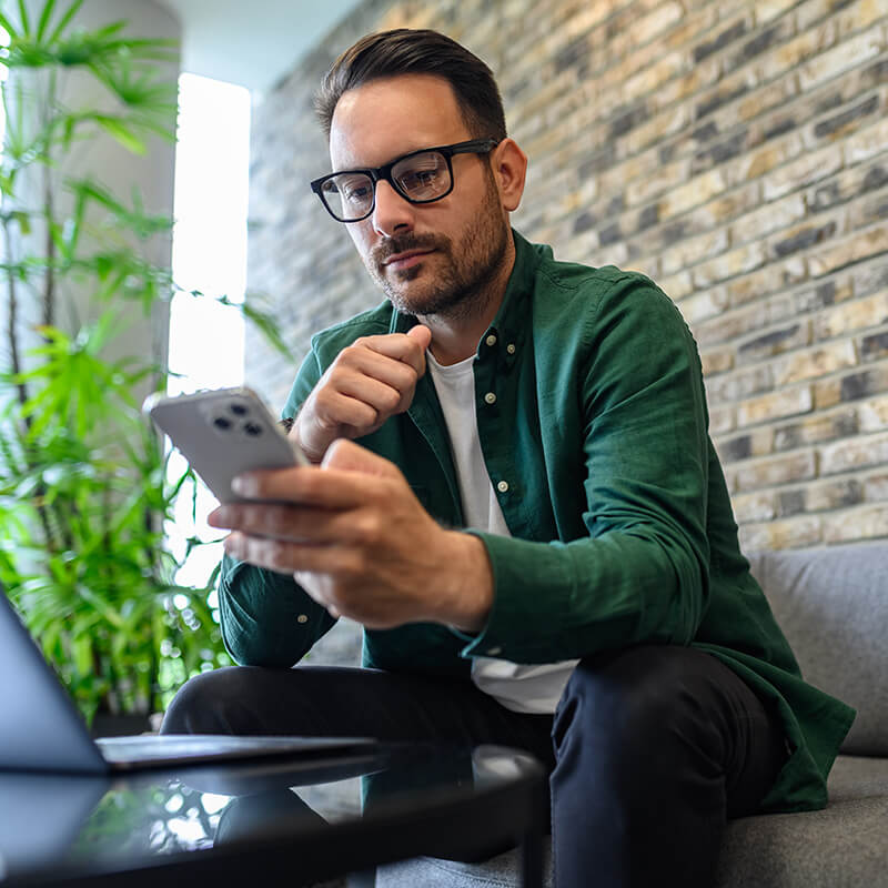 image of man looking at cell phone while sitting on couch